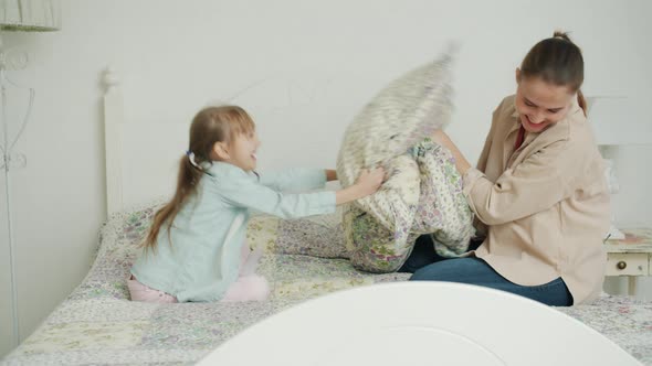 Little Girl and Loving Mother Are Fighting Pillows Laughing Relaxing in Bed at Home Together