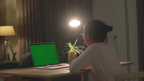 Teenage Girl Sitting At Her Desk Learning Online On A Laptop With Green Mock-Up Screen
