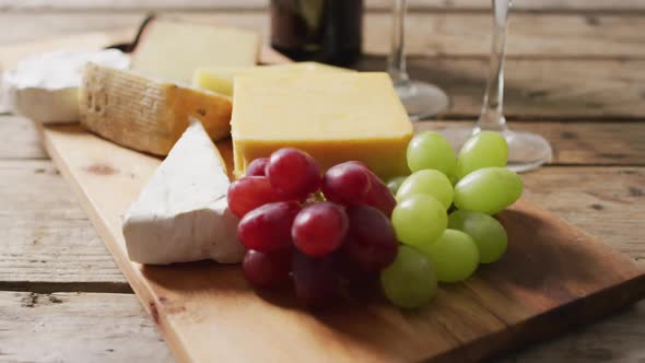 Video of diverse cheeses, grapes and glasses of wine on wooden surface