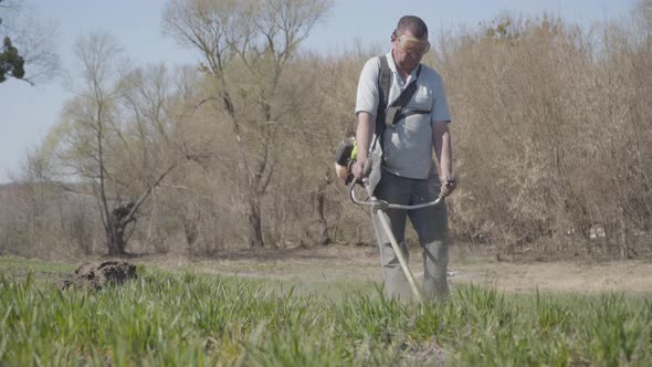 Portrait of Concentrated Caucasian Man Cutting Grass with Lawn Mower