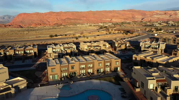 Moving forward above houses with pool and horizon of mountains and desert at sunset