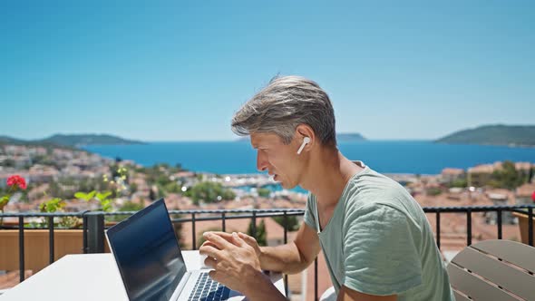 Dolly Zoom Out Footage Man in Earphones Working with Laptop Outdoors By Beautiful Blue Sea View