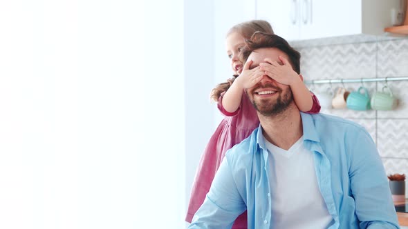 A little preschool girl covers her dad's eyes with her hands