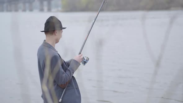 Young Fisherman in a Jacket and a Cap with a Brim in the Early Morning Catch Fish