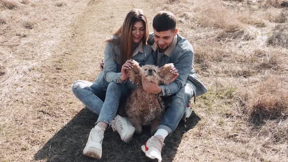 Pretty Young Woman and Man Are Sitting in the Field Walking with a Cute Dog