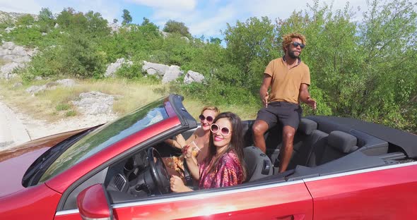 Handsome black man sitting on hood of convertible dancing with friends, graded