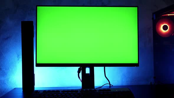 Blank green screen desktop computer on the table with RGB led lights in the dark room