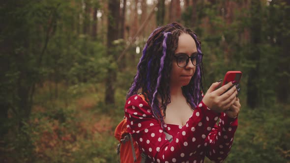 Traveling Woman with Dreadlocks with a Phone in Woods