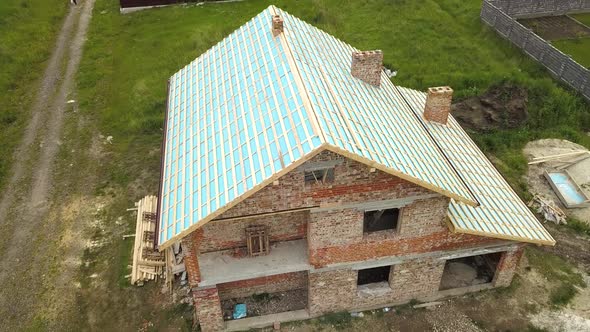 Aerial view of a brick house with wooden roof frame under construction.
