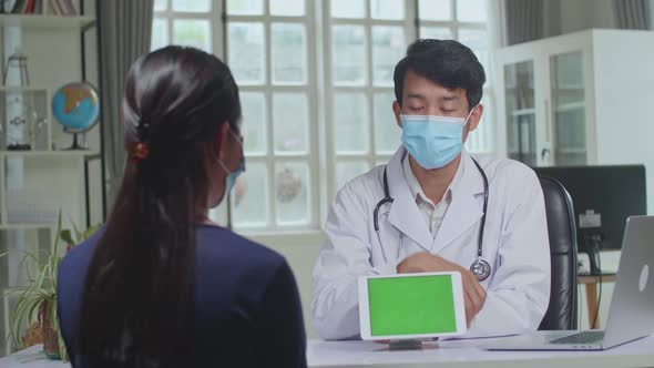 Asian Man Doctor Showing Green Screen Display On Tablet Computer During Consultation