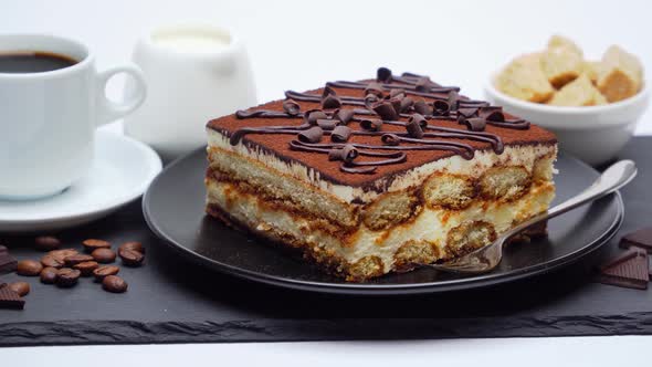 Portion of Traditional Italian Tiramisu dessert, cup of espresso and cream or milk