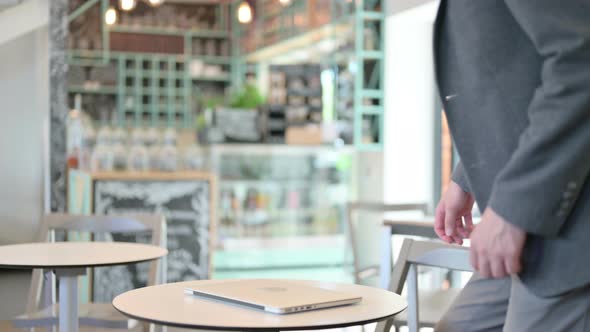 Young Man Coming Back and Opening Laptop in Cafe