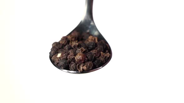 Black Pepper Peas Falling From the Iron Spoon. White Background. Slow Motion