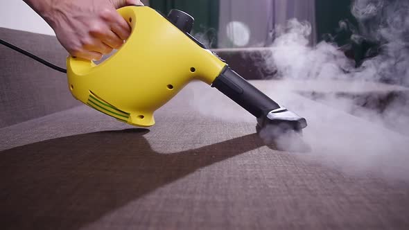 Furniture and Apartment Cleaning Concept. Man Cleaning Couch with Steam Cleaner at Home