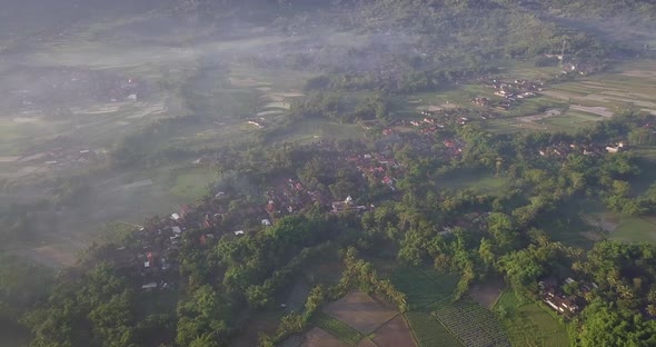 Aerial top down shot of countryside with plantation and small village in Indonesia during sunny and