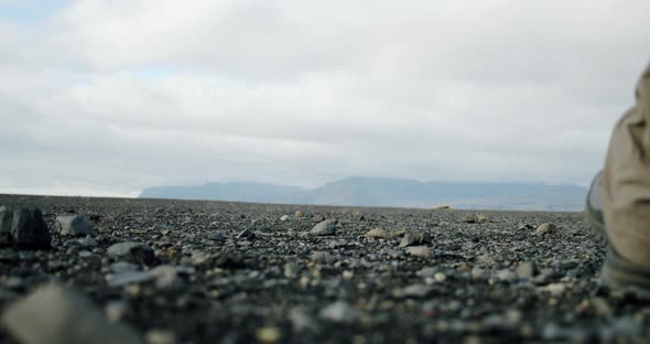 A Close Up View of a Man Legs in Boots Walking on Black Sand and Stones on a Beach in Iceland