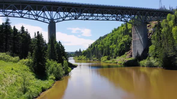 A drone flies under a bridge FPV style right above water, cars drive overhead on a large metal bridg