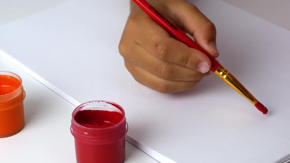 Painting with paints. The child holds a brush in his hand and dips it in red paint for painting