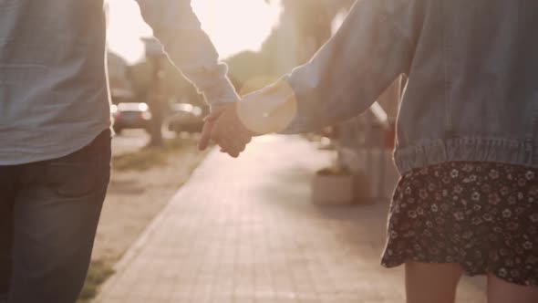 Closeup Man and Woman Hold Hands and Walk Along Street in Sunbeams of Sunset