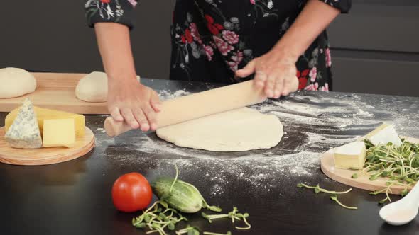 Hands roll out dough with rolling pin on wooden table