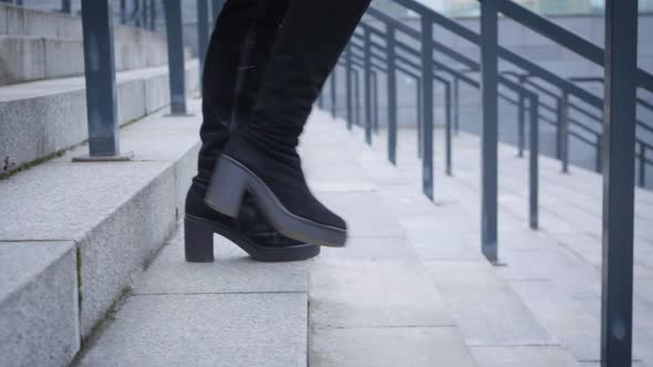 Camera Following Female Legs in High Boots Walking Down the Stairs. Woman Strolling in City