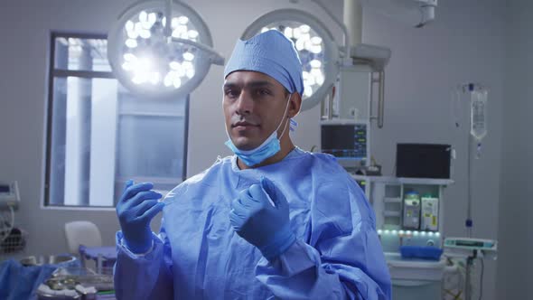 Portrait of mixed race male surgeon wearing lowered face mask smiling in operating theatre