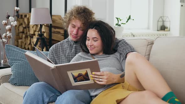 Likable Contented Married Pregnant Couple in Love Looking Family Album on the Comfortable Sofa