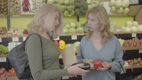 Senior Caucasian Women Discussing Eggplant and Red Bell Pepper in Grocery. Confident Housewives