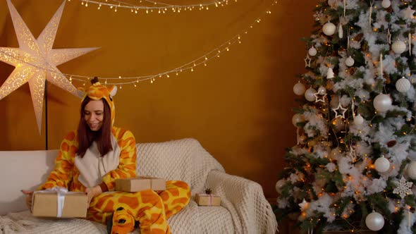 Woman in Pajamas with Gift Boxes Sitting on Couch Near Christmas Tree