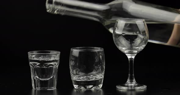 Pouring Up Three Shots of Vodka From a Bottle Into Glass. Black Background