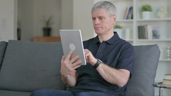 Cheerful Middle Aged Businessman Using Tablet on Sofa