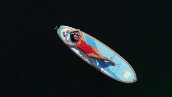 Aerial Drone View on Well Looking Middle Aged Woman with Black Hair in Red Swimsuit Swimming on Sup