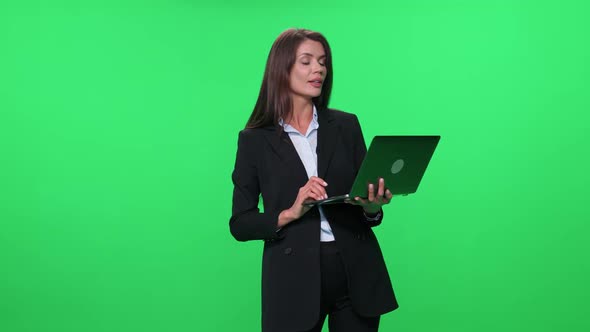 Woman Lecturer in Suit Speaks to the Audience and Give a Lecture Using a Laptop Green Background