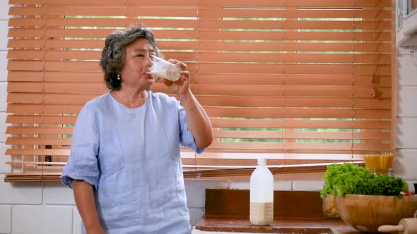 Portrait senior Asian woman drinking milk in kitchen at home.