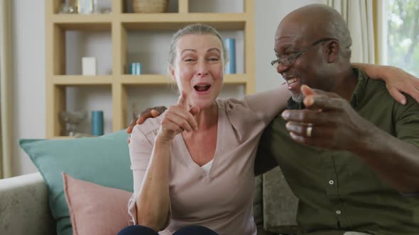 Portrait of happy senior diverse couple wearing shirts and making video call in living room