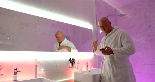 Bald Man in a White Coat Is in the Spacious Bathroom. He Makes Dance Gestures with His Hand