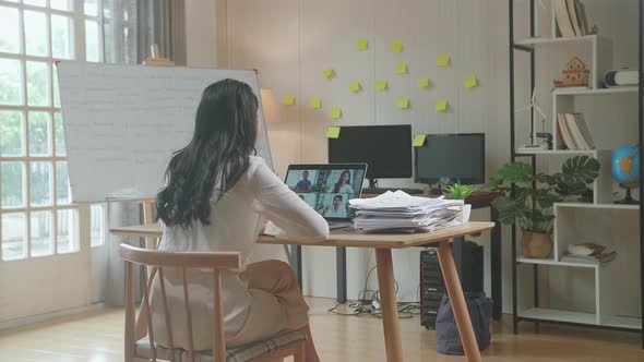 Back View Of Asian Woman Having Video Call On Laptop While Working With Documents At The Office