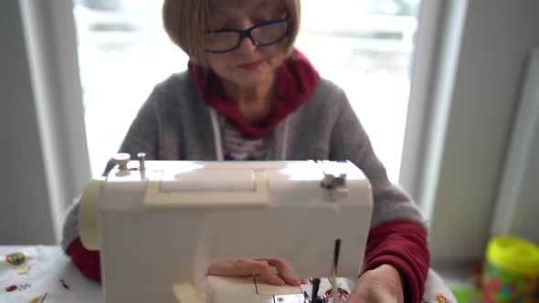 Pensioner Woman Wearing Glasses Sews Home Textiles on a Sewing Machine