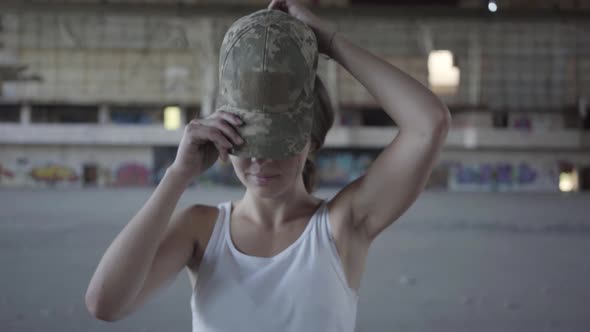 Portrait of Pretty Young Woman Putting on Military Cap on Her Head and Looking in the Camera