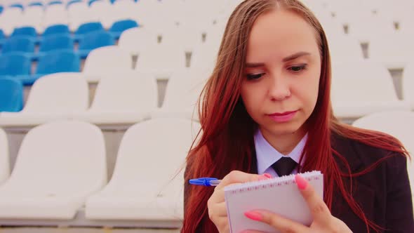 Young Woman with Notepad Pen Sitting on Stadium Bleachers Alone