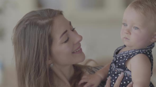 Portrait of a Beautiful Mom and Cute Baby Indoors Together. Caucasian Mother Holds a Baby in Her