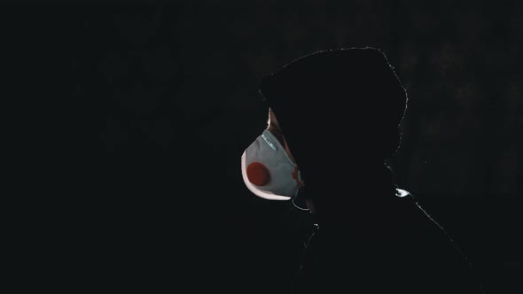 Silhouette of Man in Hood and Medical Mask Watching TV with Fake News. Pandemic