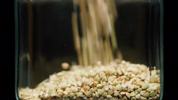 Closeup of Falling Down Green Buckwheat Into Glass Jar on Black Background