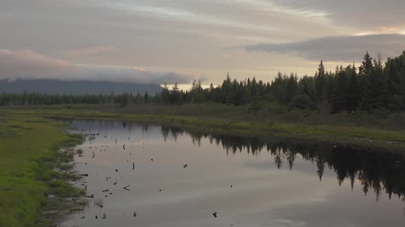 Slow cinematic aerial over reflective calm river sunrise over mountain wilderness