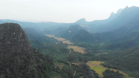 Aerial: flying over rice paddies unique valley scenic cliffs rock pinnacles tropical jungle Laos