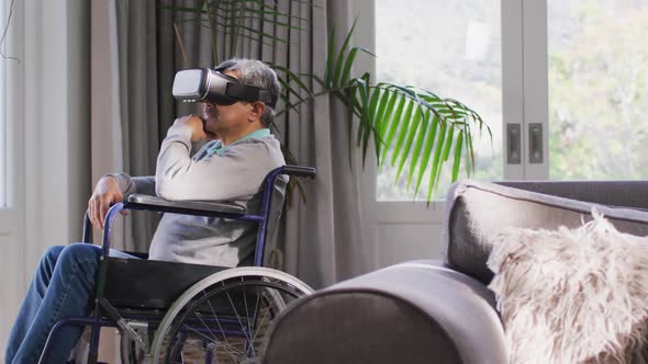 Happy mixed race senior man on wheelchair wearing vr headset and having fun at home