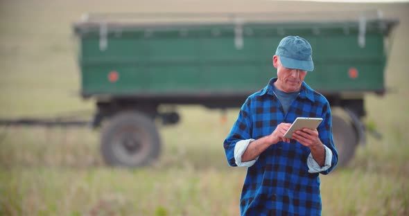 Farmer Using Digital Tablet While Looking at Tractor in Farm