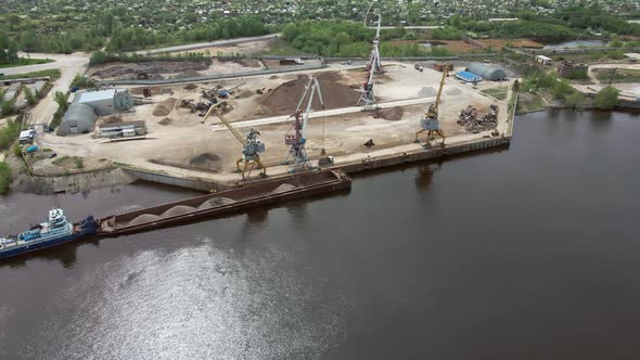 Large Harbor Cranes Onshore at the Quay Unload a River Gravel Barge Onto a Large Pile