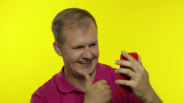 Young Caucasian Man Posing in Pink T-shirt. Handsome Guy Using Mobile Phone and Win Something