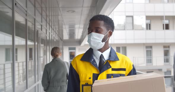 Afroamerican Courier in Safety Mask Delivery Package in Modern Office Building